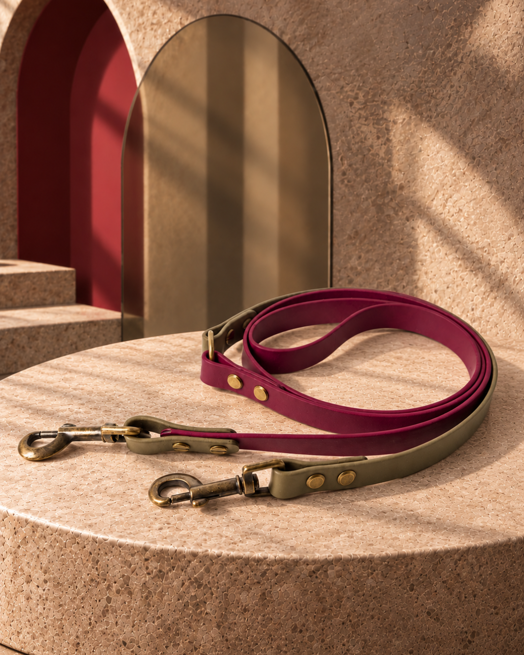 Wine-and-olive MOVE leash with two antique brass snap hooks, arranged on a warm stone surface.