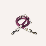 BioThane® original waterproof material, a purple leather dog leash with silver-toned metal hardware and black swivel clips, coiled on a light cream background.