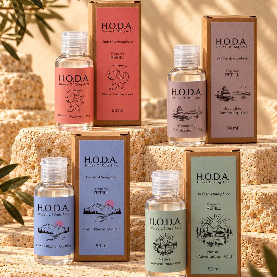 Six HODA indoor atmosphere refill bottles and matching boxes arranged on stone blocks outdoors, with olive branches framing the scene. The products come in pink, blue, beige, and green packaging with clear bottles containing clear or pale liquid.