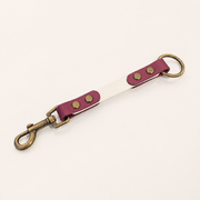 A BioThane® strap keychain or bag charm with a brass clasp and ring, featuring a white center stripe and magenta BioThane® ends with brass rivets.